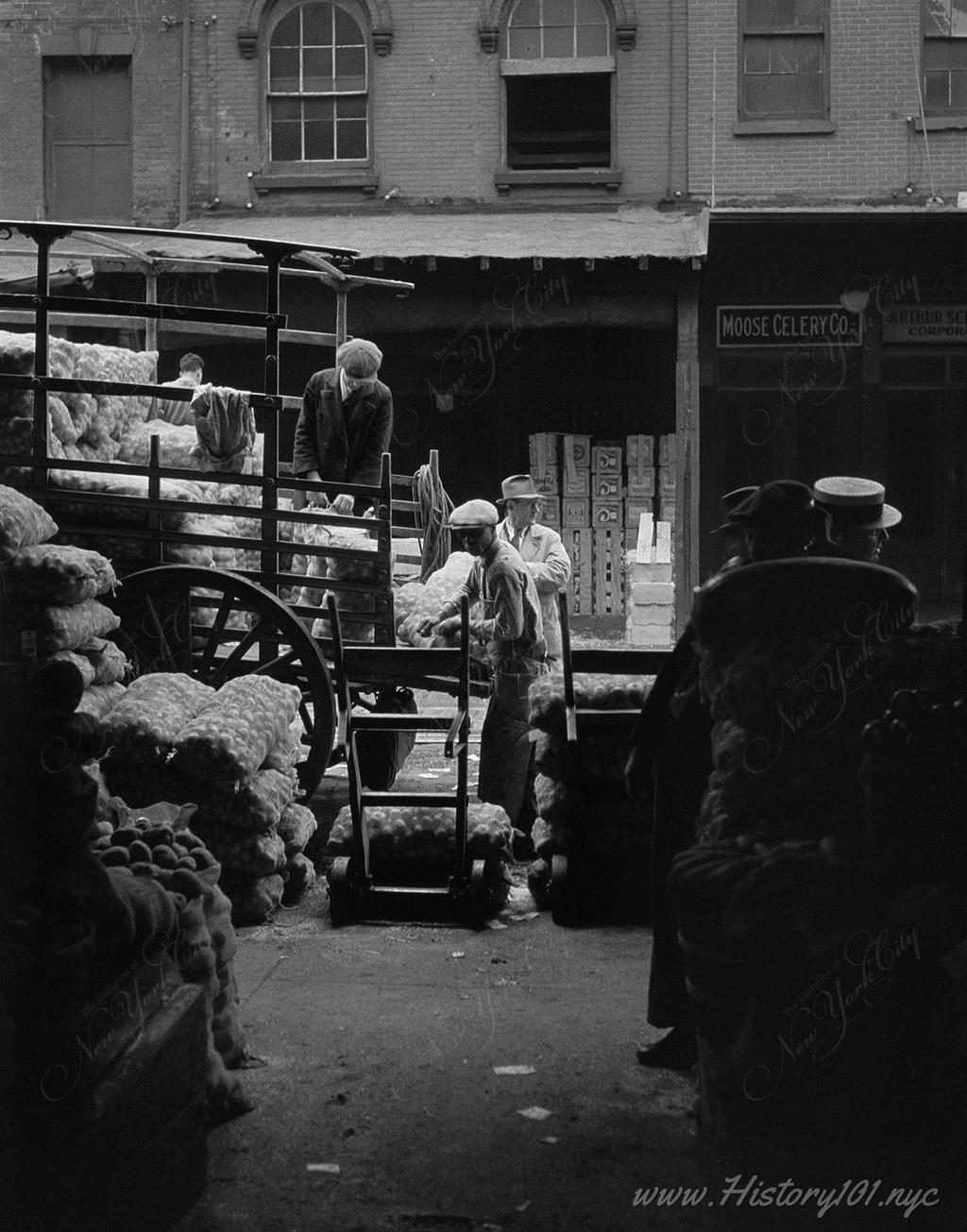 Photograph of workers unloading trucks with dollies at a downtown Manhattan market.