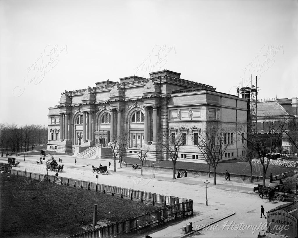 Photograph of The Metropolitan Museum of Art, founded in 1870. In the foreground a busy street filled with pedestrians, horses and carriages.