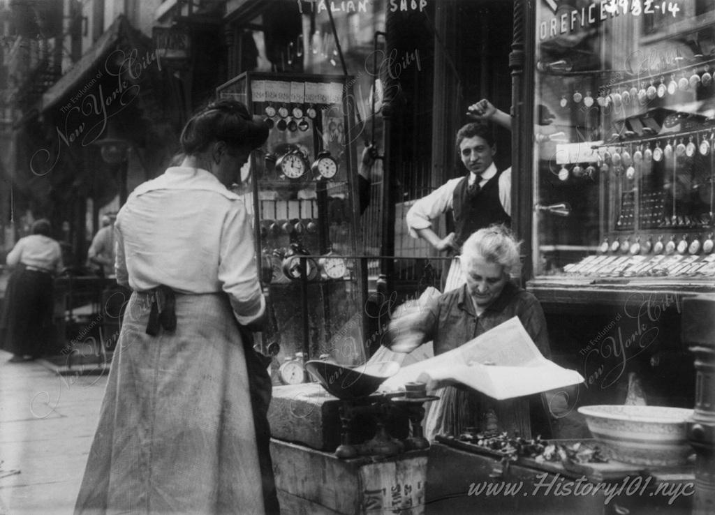 Photograph of an Italian watchmaker's shop. An older woman reads the newspaper as a pedestrian observes.