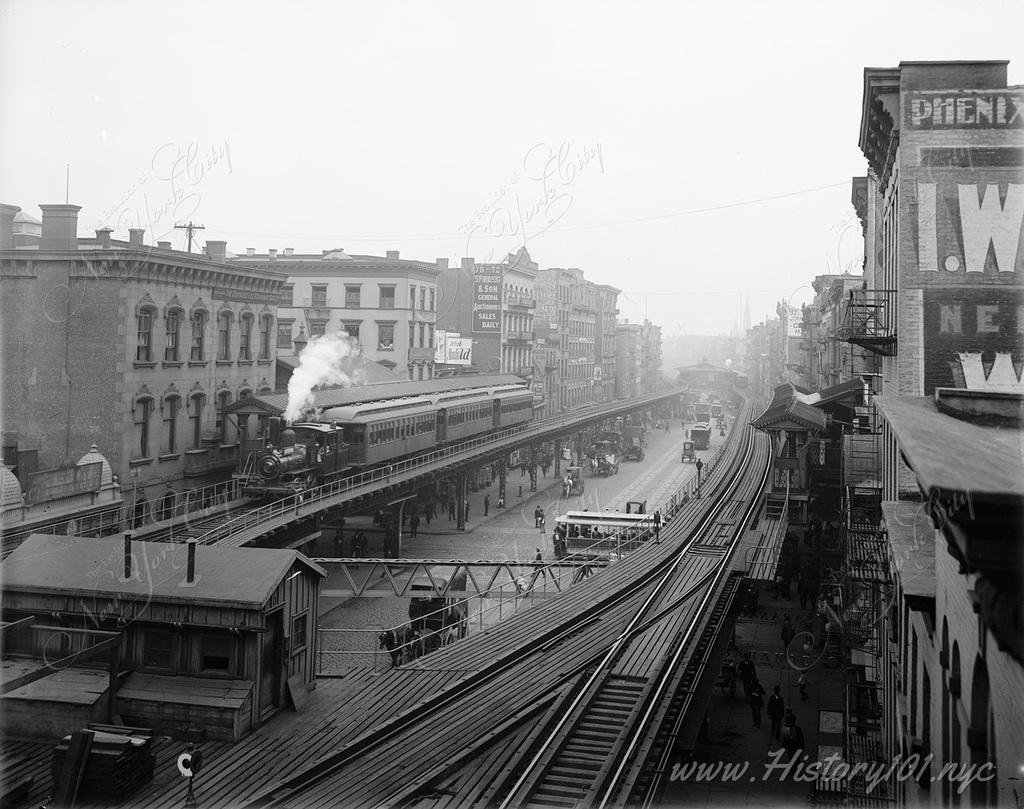 A steam-powered locomotive awaits boarding passengers on the Bowery's elevated train line near Grand Street.