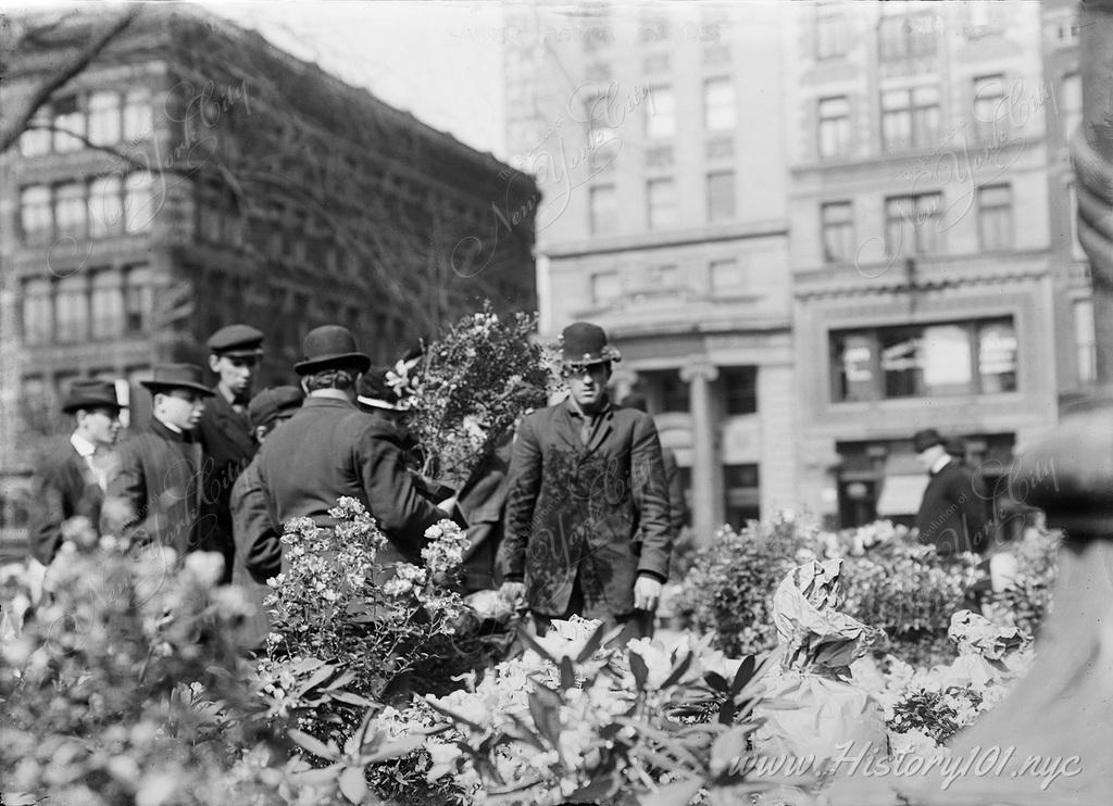 Photograph of a man selling flowers to customers, framed by large bouquets against the iconic backdrop of the surrounding buildings.