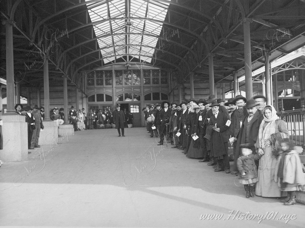 A line of immigrants has passed all phases of inspection at Ellis Island and await the ferry to Manhattan where they will begin their new lives.