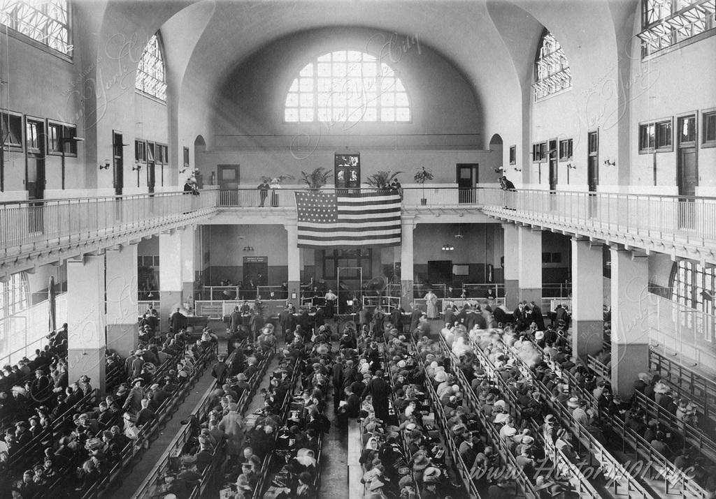 Interior view of immigrants seated on long benches and awaiting processing at the Main Hall of the Immigration Station at Ellis Island