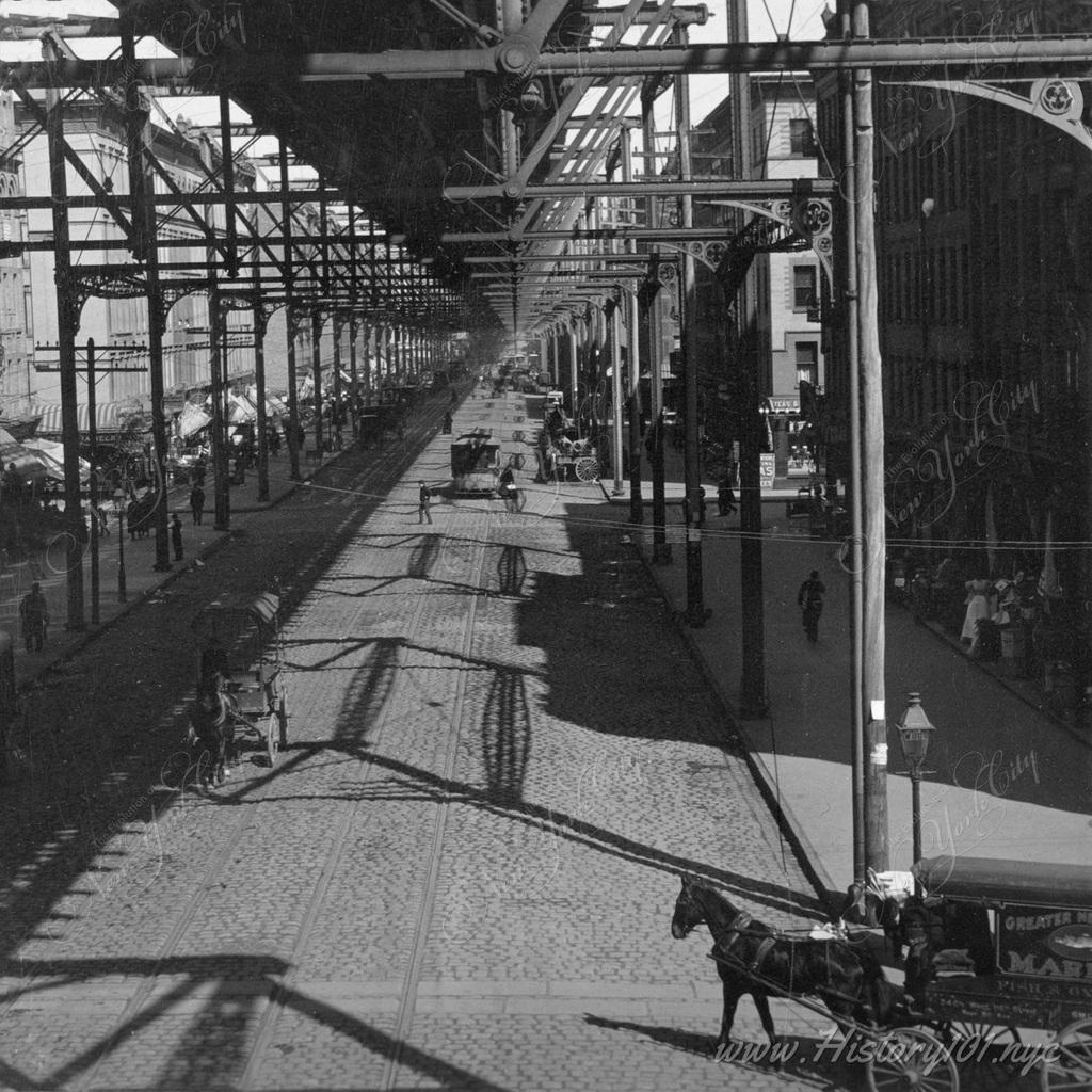 Horses and carriages move along the underpass of the elevated train tracks following 8th Avenue.