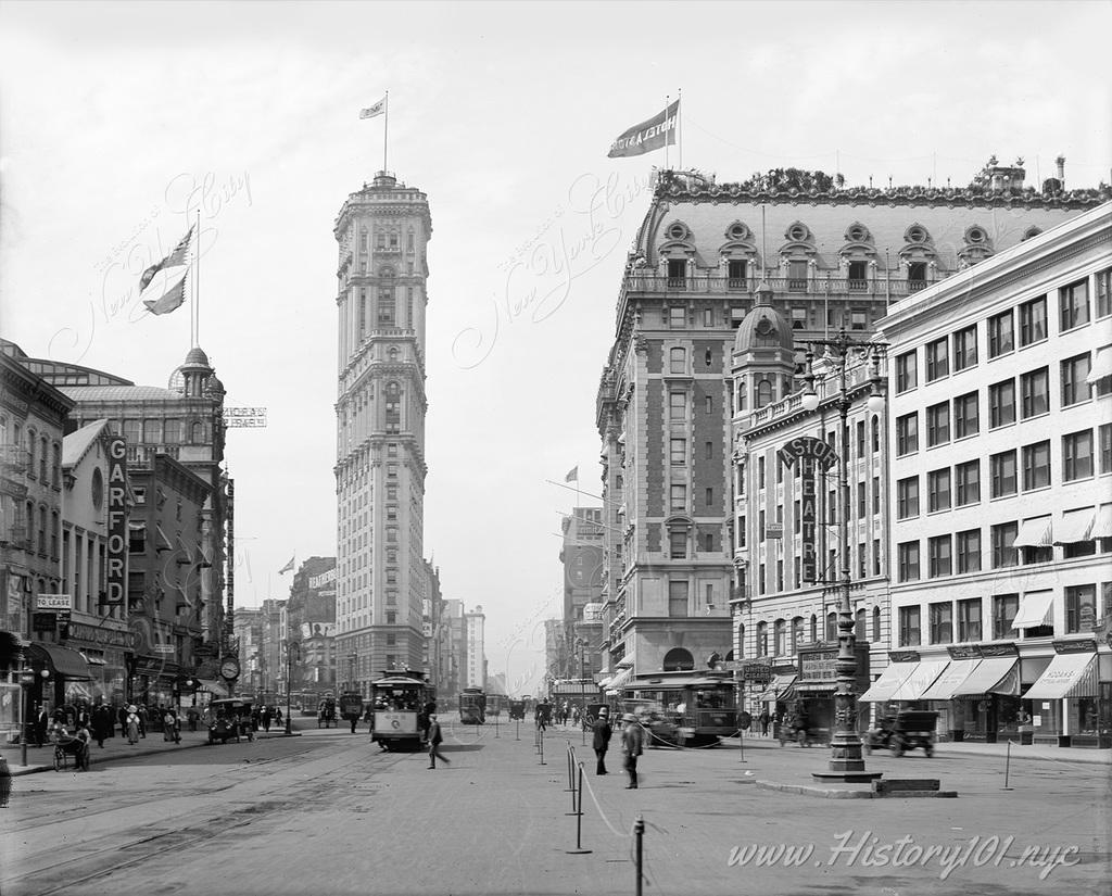 A daytime photograph of Times Square and the New Times Building, with pedestrians and trolleys in the foreground.