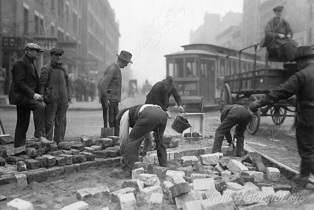 Photograph of construction workers repairing granite stonework for the pavement on a New York City street.