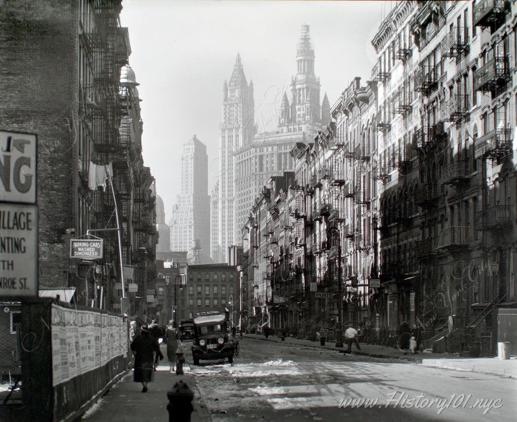 A street level view of Henry Street and Manhattan's growing skyline. City Hall and the Woolworth Building are visible in the distance.