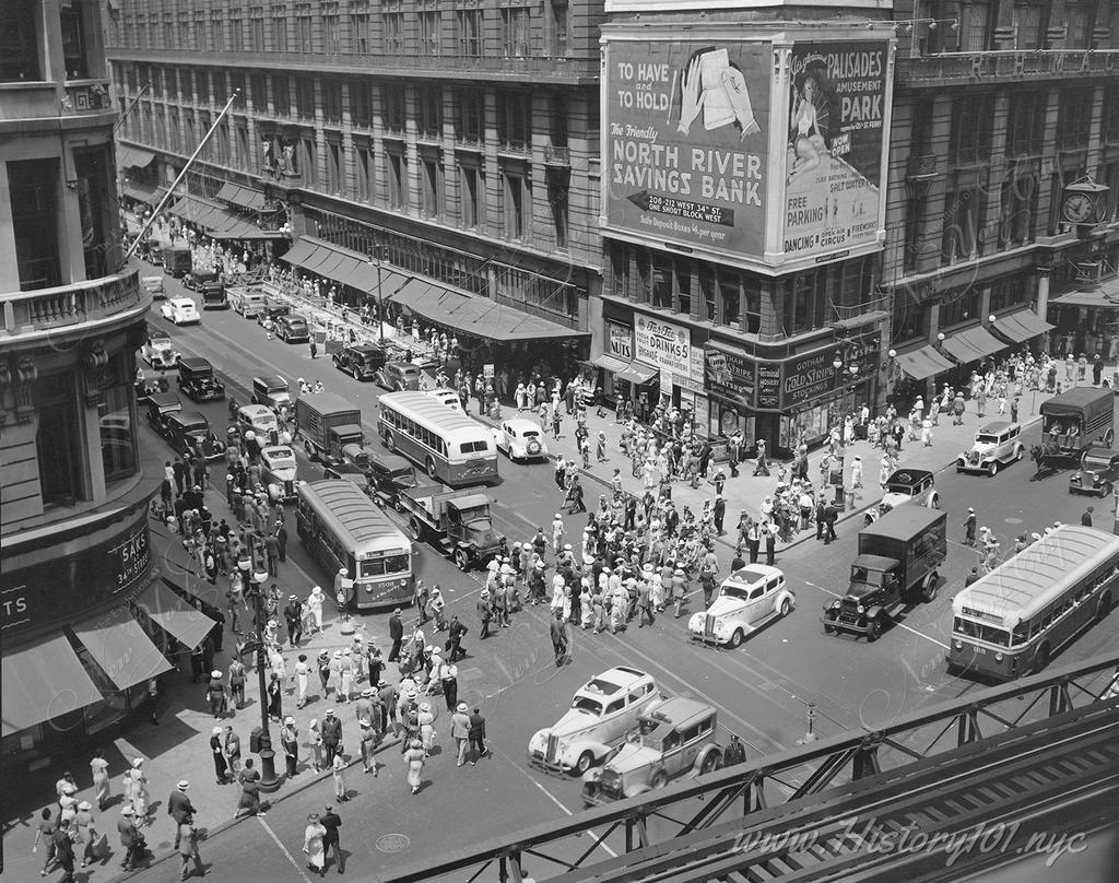 An overhead view of Herald Square the corner of  34th Street and Broadway showing cars, pedestrians and elevated railroad tracks in the foreground.