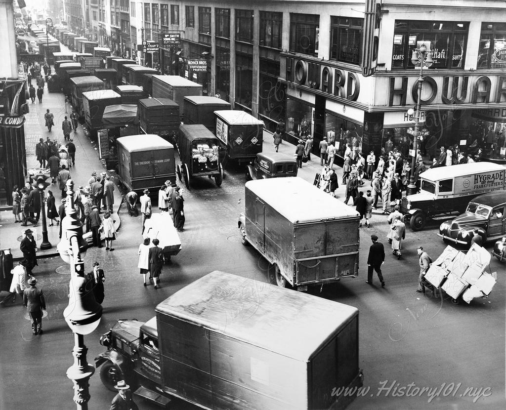 Long lines of delivery trucks stall traffic on the corner of West 37th Street, looking west from 7th Avenue, in front of Howard Clothes store.