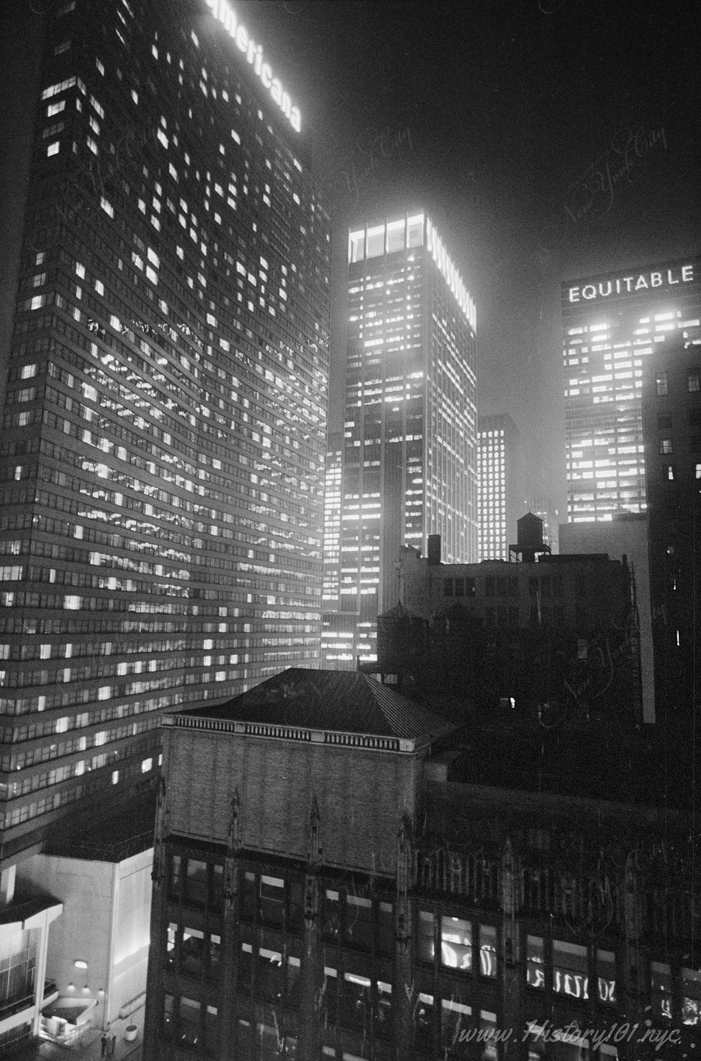 Photograph of the Equitable Building and surrounding skyscrapers and Manhattan rooftops illuminated at night.