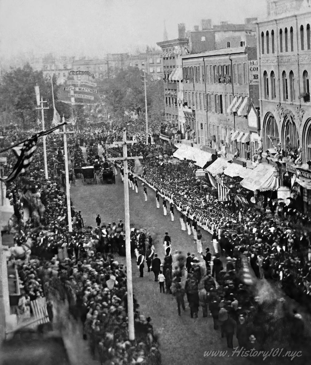 An aerial photograph shows a large crowd of spectators enjoying a parade on Broadway.