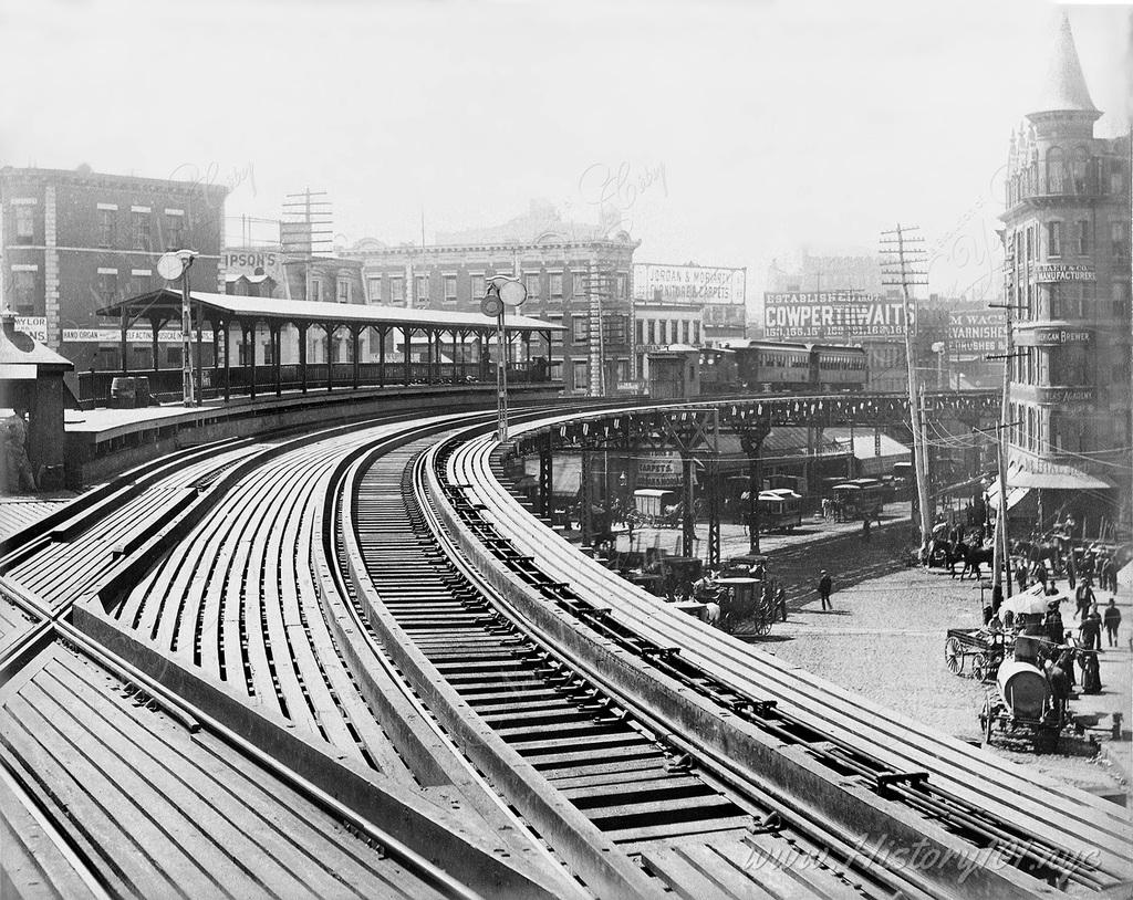 A view looking down elevated railroad tracks. A train is approaching around the curve.