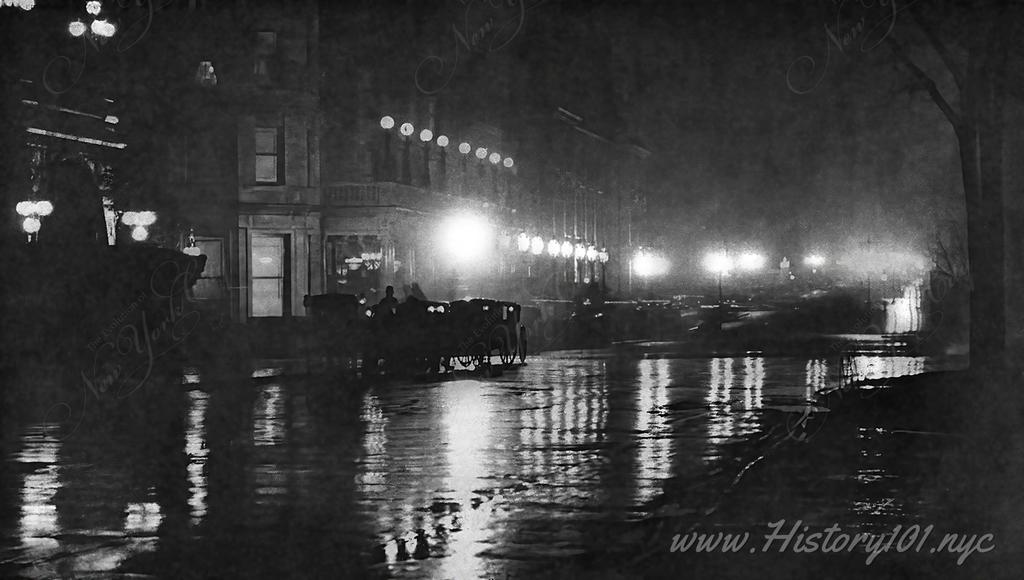 Photograph of a rain soaked street, illuminated by streetlamps which are reflected on the ground.