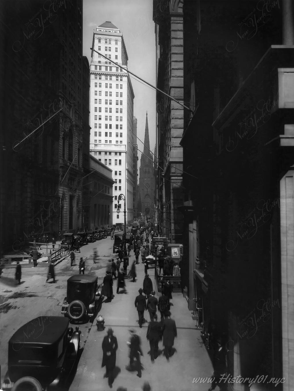 A photograph of pedestrians on Wall Street with Trinity Church in the background.