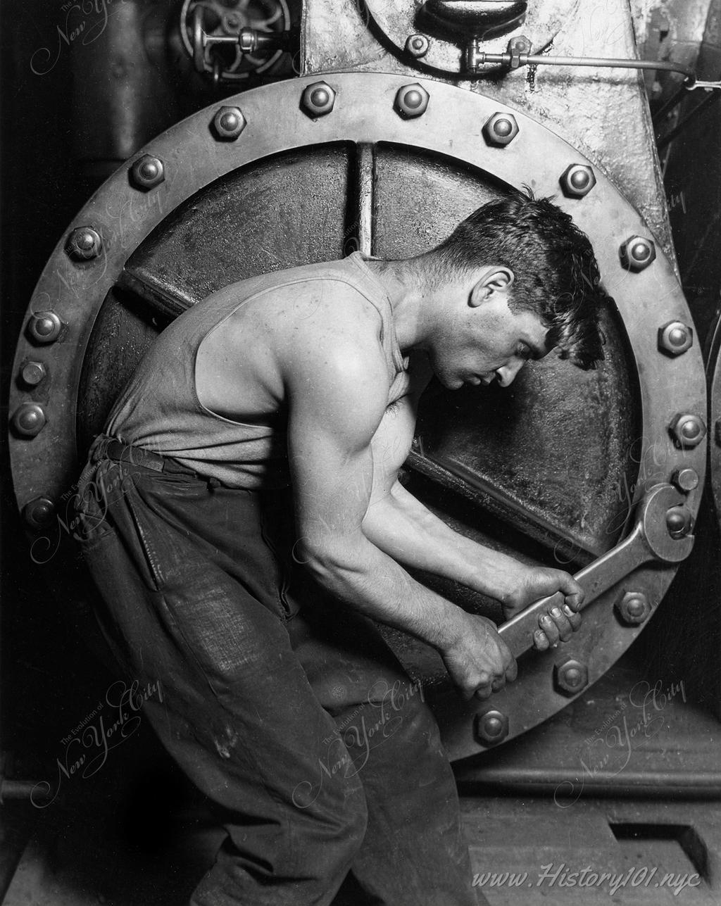 Photograph of a young mechanic tightening the bolts of a steam pump with a wrench.