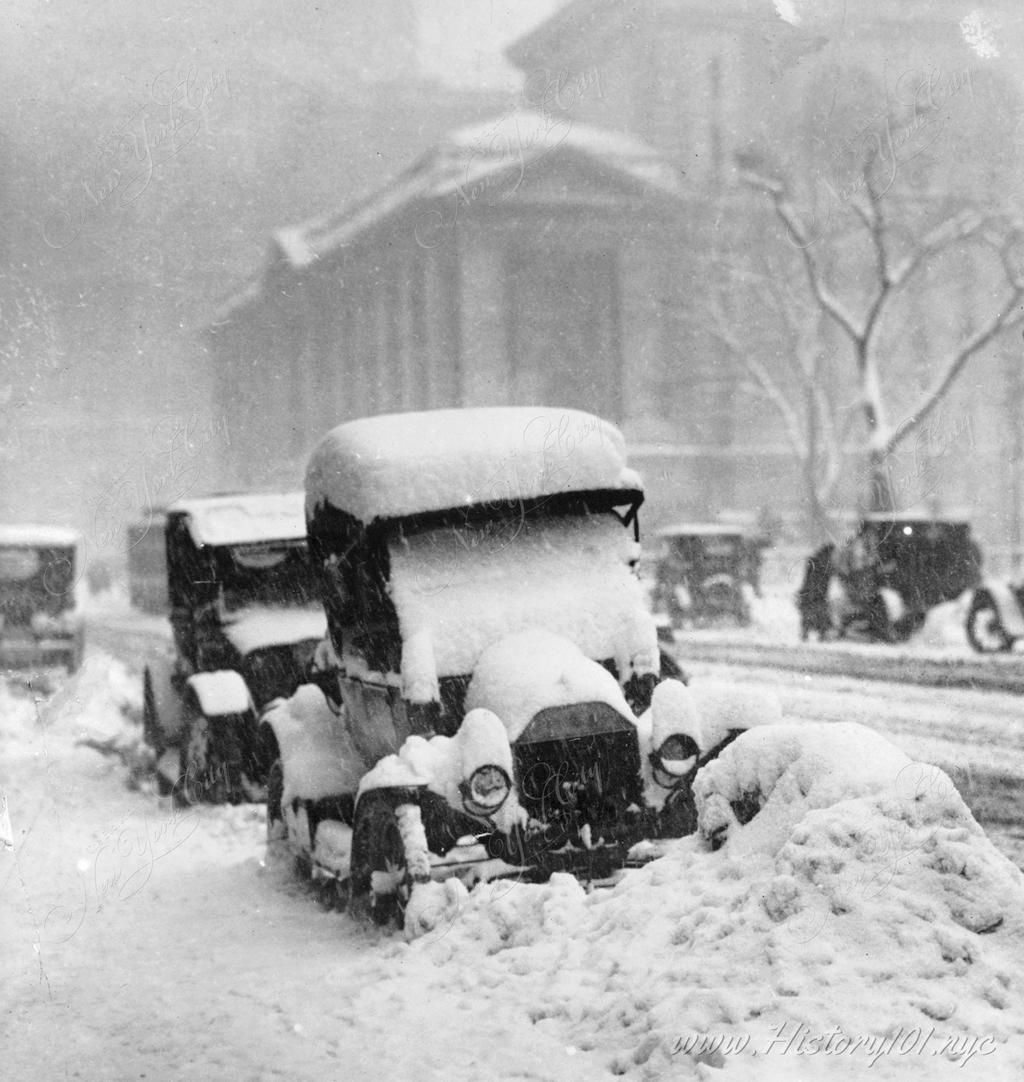 Photograph of parked cars, locked in place by piles of snow after a blizzard.