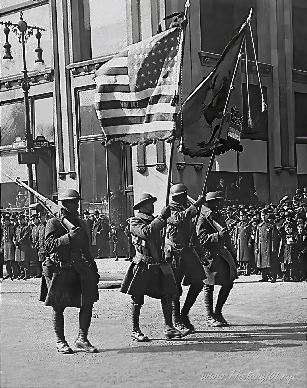 Photograph of the 369th Infantry, commonly referred to as "The Harlem Hellfighters" waving an American flag and their infantry colors.
