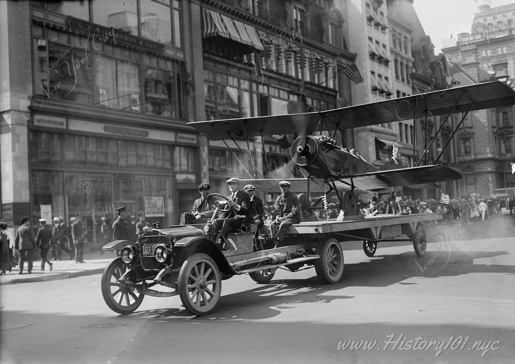 Photograph shows a Fourth of July parade on Fifth Avenue, New York City in 1918 with a Curtiss bombing plane mounted on a truck.
