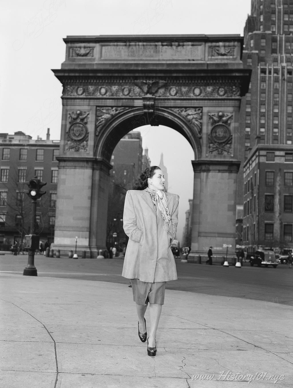 Photograph of Ann Hathaway posing in front of the  Washington Square Arch of Triumph with the 5th Ave skyline and a glimpse of the Empire State Building.
