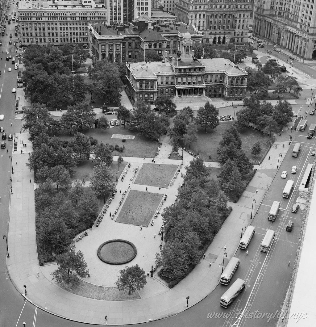 Photograph shows view of Broadway looking south from above the 135 highway with large skyscraper in distance and subway tracks emerging from the ground.