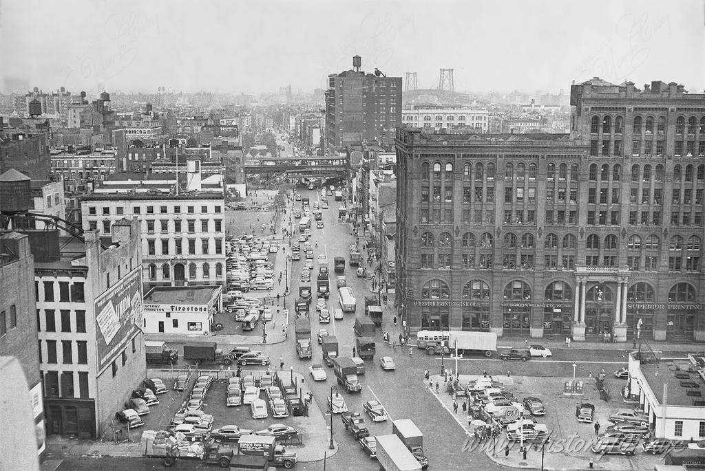 Photograph shows busy intersection at Houston Street looking east from Broadway. An elevated train track visible in the background.