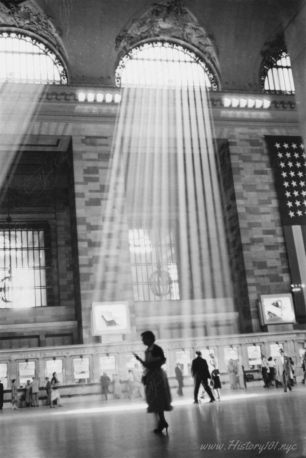 Photograph shows the interior of main concourse of Grand Central Terminal with sunlight streaming through windows of main concourse.