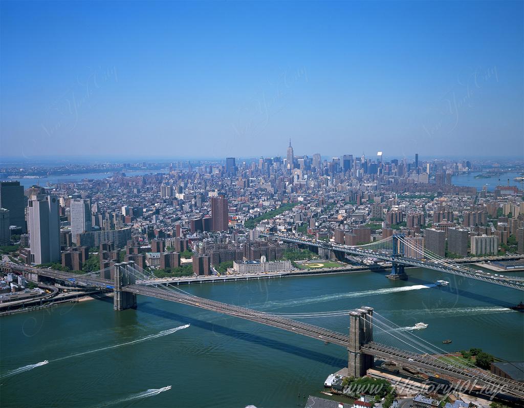 Aerial photograph above the East River Shows the Brooklyn and Manhattan Bridges with Midtown's skyline visible in the distance.