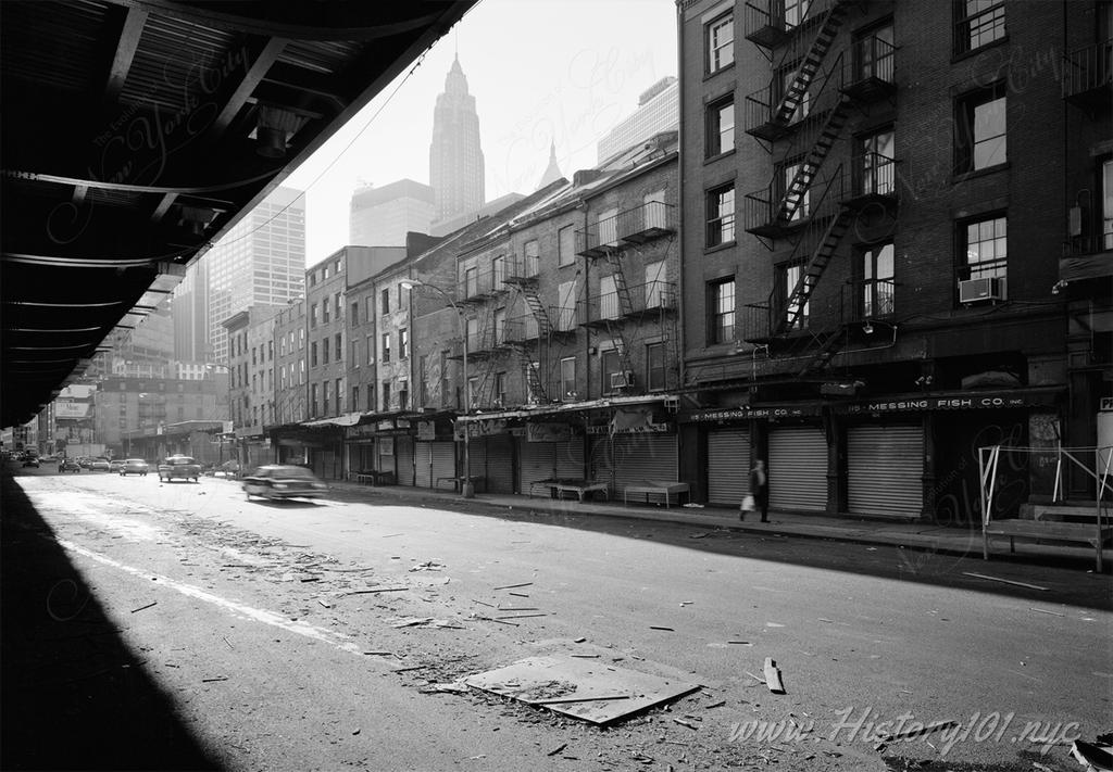 Photograph of traffic in South Street Seaport with the Woolworth Building visible in the background.