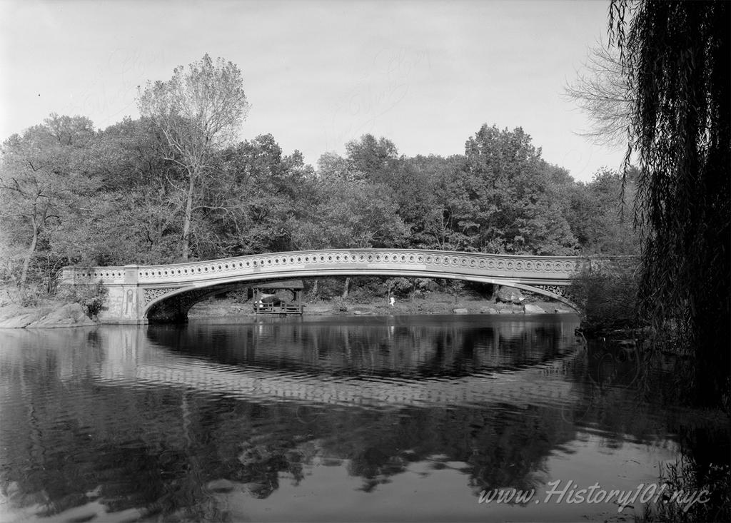 Photograph of Central Park's Bow Bridge. One of the park's many rustic pavilions is visible under the left side of the arch.