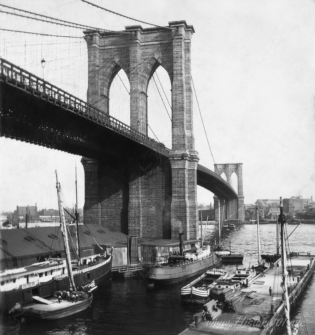 Photograph of boats in the East River docked near the Brooklyn Bridge.