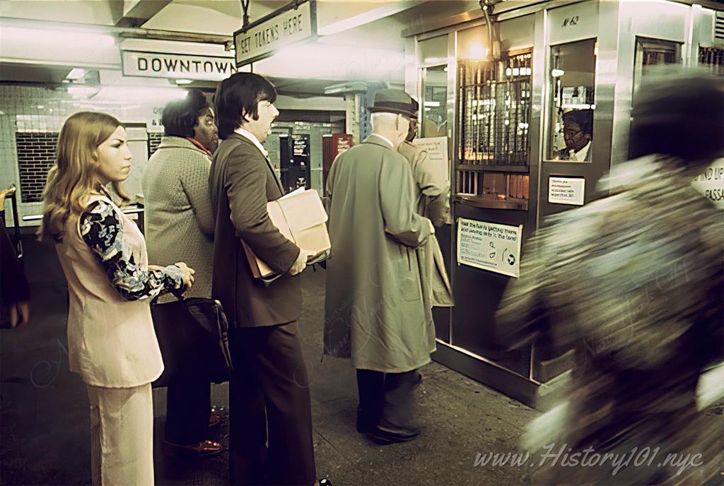 Photograph of passengers waiting in line to buy tokens at a subway station booth.