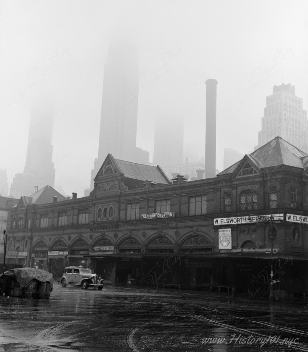 Photograph of the Fulton Fish Market, with downtown skyscrapers barely visible in the morning fog.
