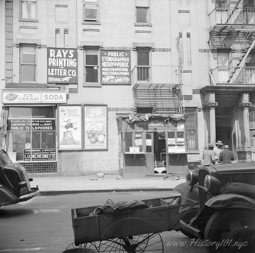 Photograph of a diner, shoeshine booth and various printed advertisements near the corner of a block in Harlem.
