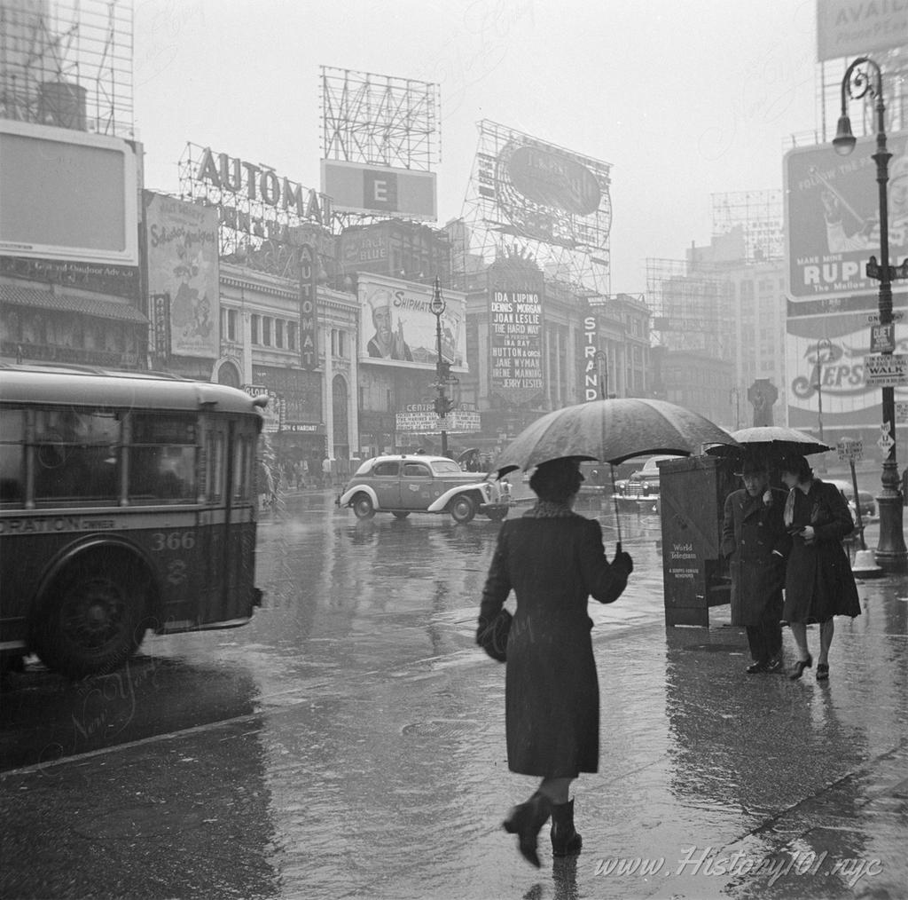 Photograph of traffic and pedestrians with umbrellas walking along Times Square in midtown Manhattan.