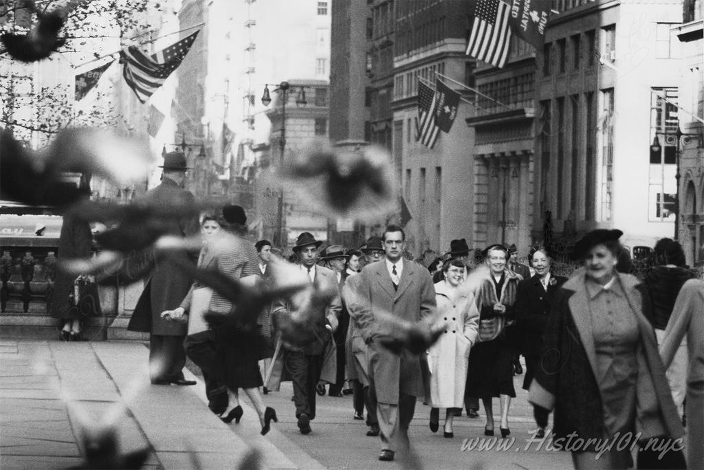 Photograph of pedestrians scattering a flock of pigeons along the sidewalk in front of New York Public Library.