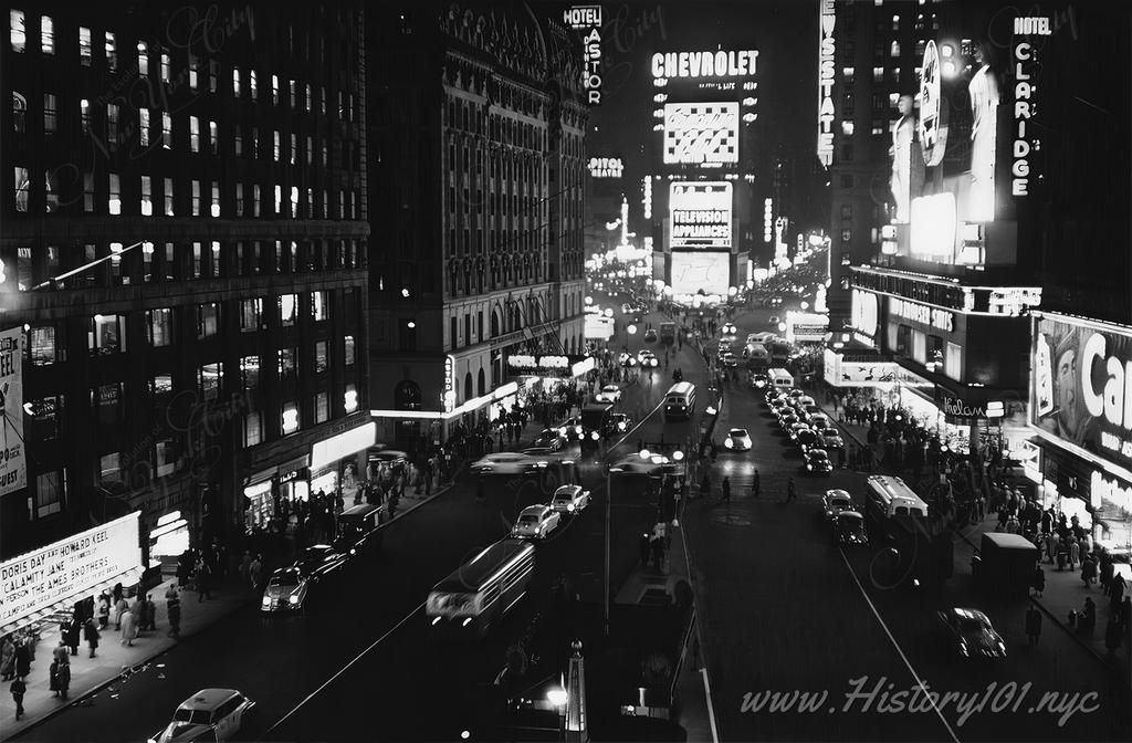 Aerial Photograph of a busy night in Times Square, illuminated by its many billboards, storefronts and the lights of passing traffic.