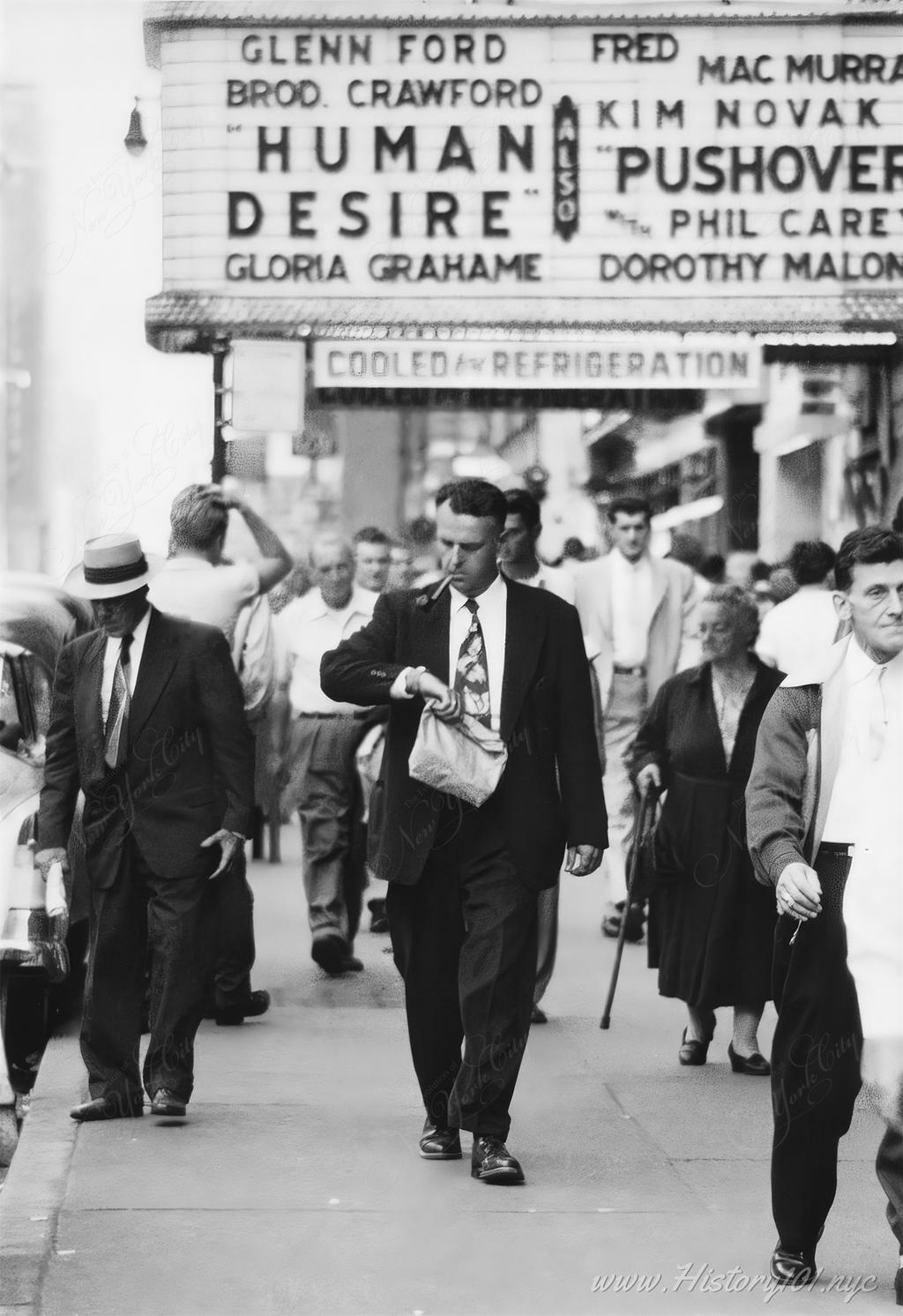 Photograph of people walking on a Manhattan sidewalk with several theatre marquees visible in the background.