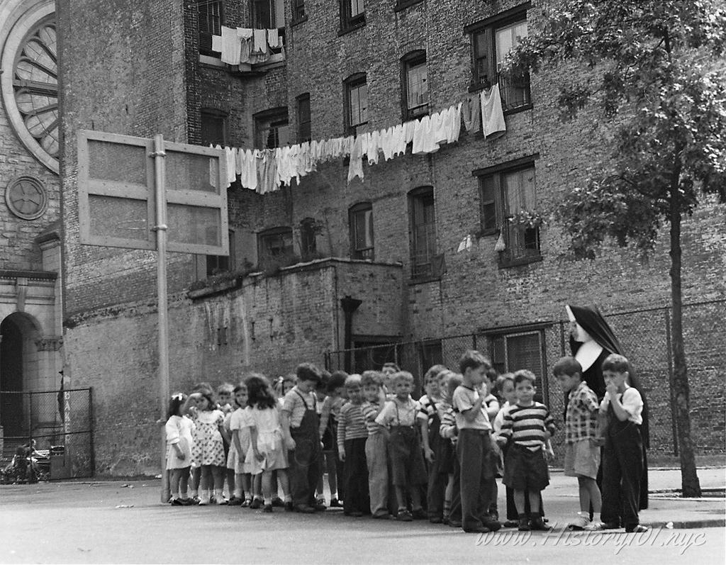 Photograph shows a nun with a group of children on the basketball court at Saint Anthony's playground.