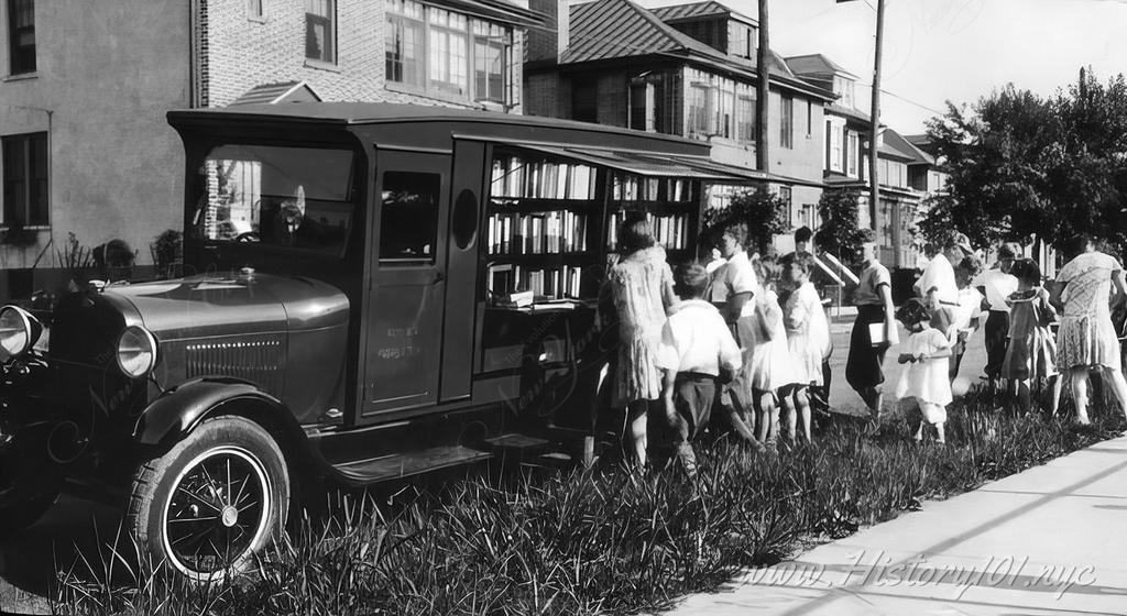 Photograph of a traveling library parked on a grassy verge in the Bronx, with a line of kids waiting to check out some books.