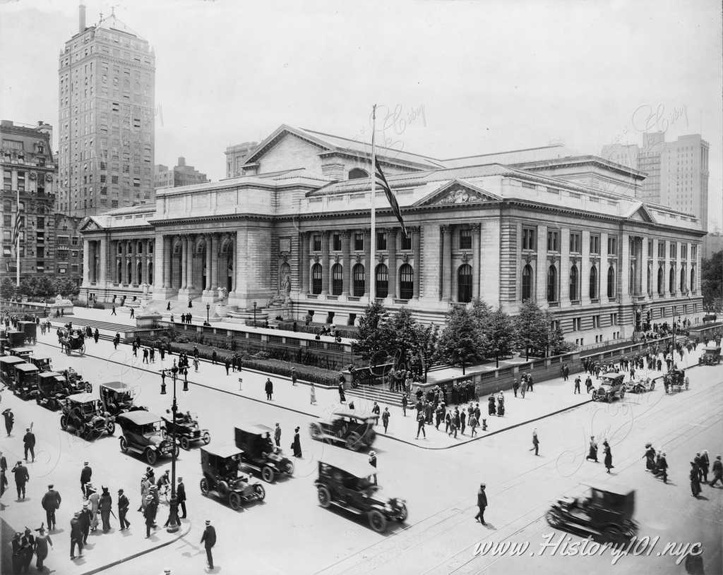 New York Public Library as seen from a building across intersection of East 42nd Street and Fifth Avenue, showing the front and east facades, as well as automobile and pedestrian traffic.