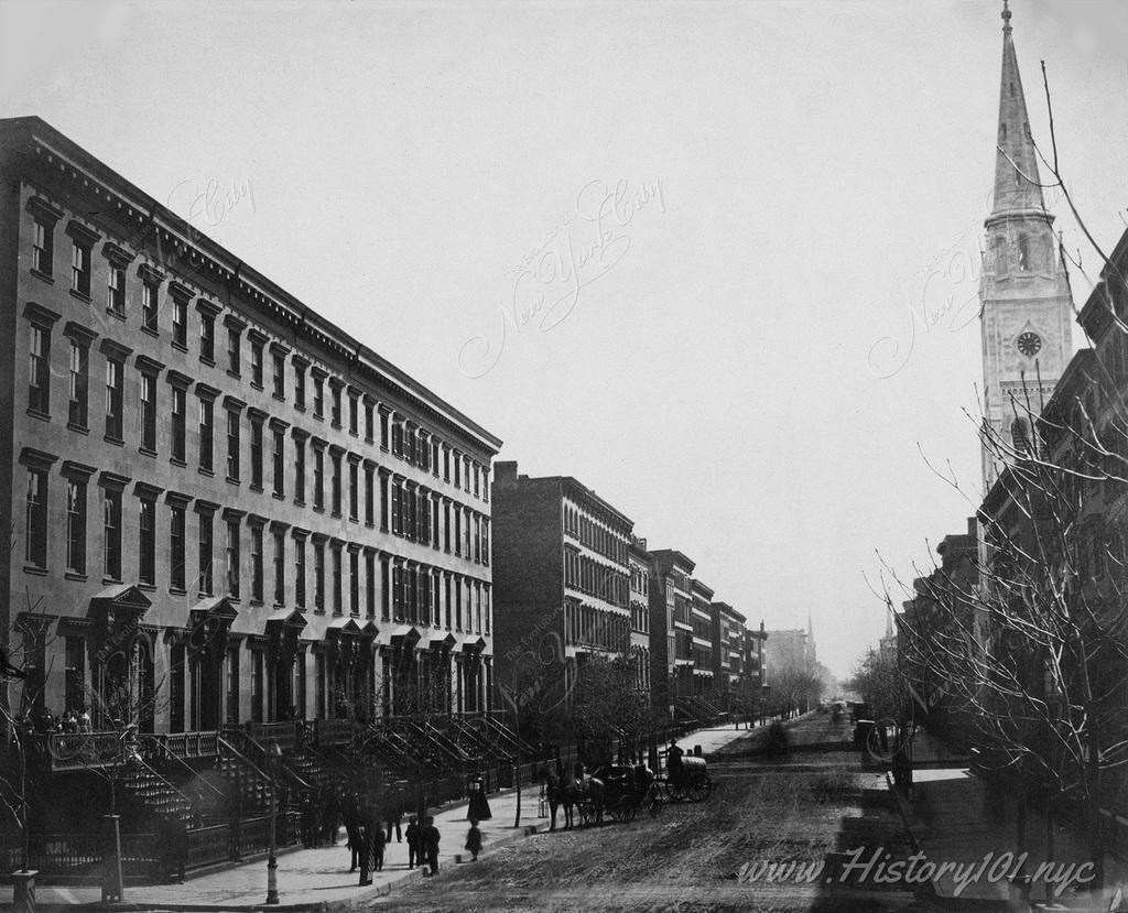 View of a residential neighborhood along New York's Fifth Avenue. Rows of single-family brownstones with grand front stoops line the wide corridor.