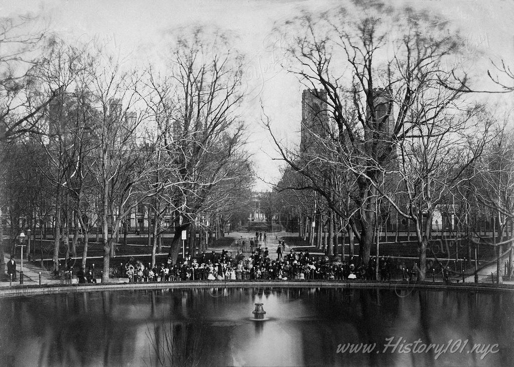 A group portrait photograph of men, women & children gathered in front of Washington Square Park's famous fountain.