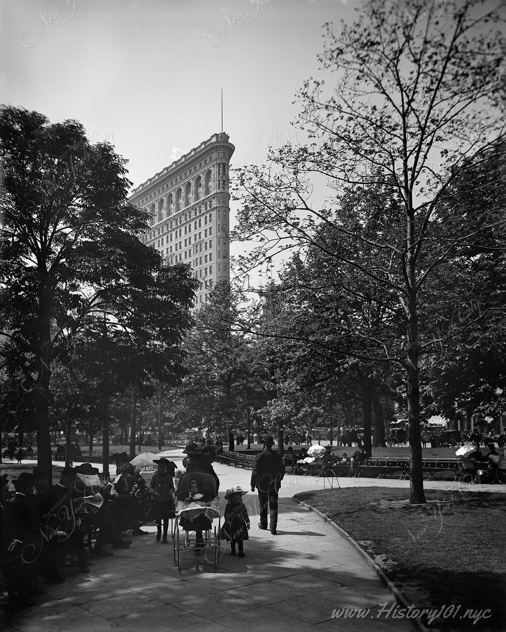 Families stroll through Madison Square Park, its trees framing the recently completed Flatiron Building.